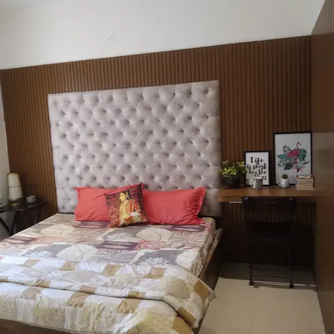 Bedroom with a tall tufted taupe headboard against a fluted wood-panel wall, coral pillows