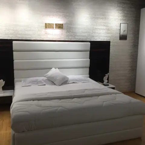 Bedroom with a tall white channel-upholstered headboard set against high-gloss dark macassar wall panels
