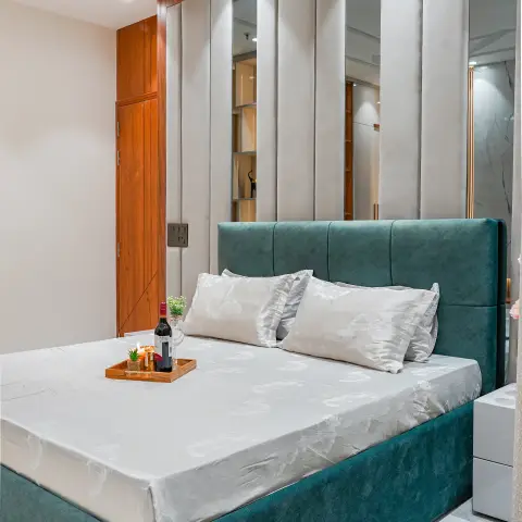Bedroom with a teal channel-tufted upholstered bed against a fluted mirror-and-fabric panel headboard wall lit by cove lighting
