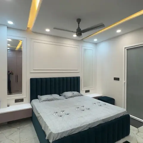 Bedroom with a teal channel-tufted upholstered bed against a white panel-moulded wall under a cove-lit ceiling with a ceiling fan.