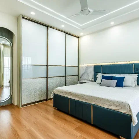 Bedroom with a teal channel-tufted upholstered bed against a marble-pattern wallpaper headboard wall, a mirrored glass sliding-door wardrobe