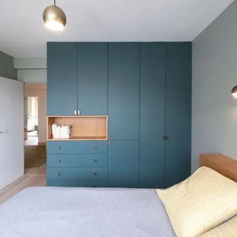 Bedroom with a teal fitted wardrobe wall that steps down into a three-drawer chest and an oak-lined open niche