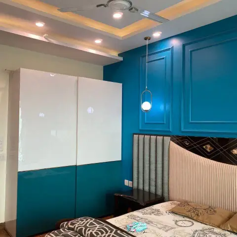 Bedroom with a teal moulded panel accent wall behind a channel-tufted headboard, a drop pendant light, and a cove-lit stepped POP ceiling