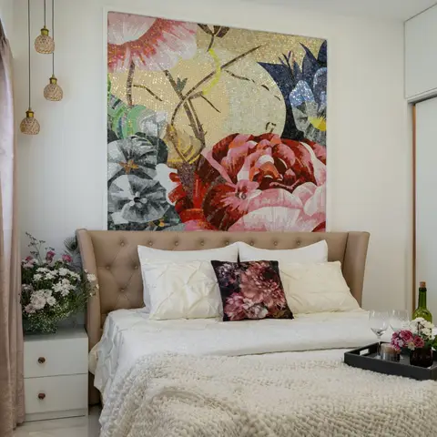 Bedroom with a tufted taupe leather wingback headboard beneath a large floral mosaic wall art panel, glass pendant lights, and a styled bedside tray.