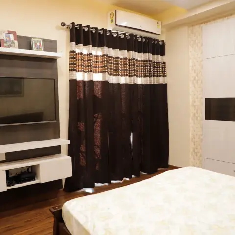 Bedroom with a wall-hung white-and-wenge TV panel carrying framed deity prints on its top shelf