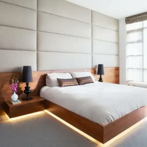 Bedroom with a walnut platform bed featuring built-in under-bed LED lighting and integrated floating nightstands, set against a cream upholstered panel wall.