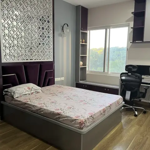 Bedroom with a white CNC-cut jaali panel set into a glossy aubergine headboard wall, purple velvet headboard cushions over a grey storage bed