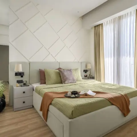 Bedroom with a white diamond-lattice moulded headboard wall, a cream upholstered bed dressed in a sage quilt with a rust throw and a tea tray