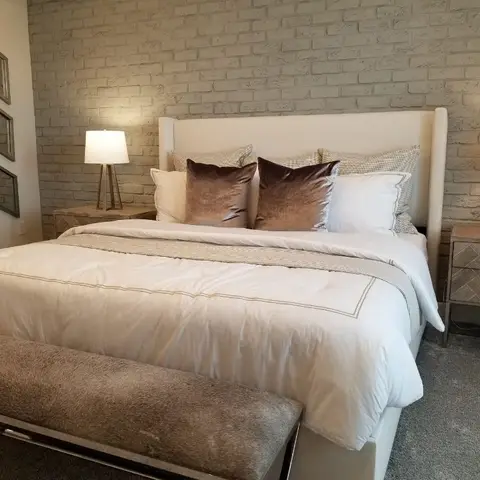 Bedroom with a whitewashed exposed-brick accent wall, an upholstered wingback headboard flanked by matching lamps, and a trio of arrow-shaped mirrors