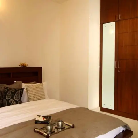 Bedroom with a wide wood headboard wall unit, a dark wood wardrobe with frosted glass panel inserts, and a breakfast tray staged on the bed.