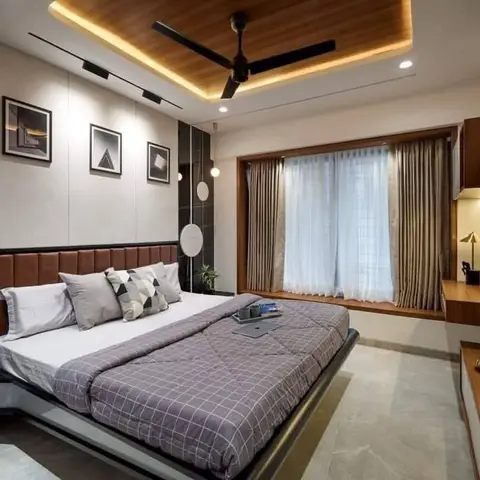Bedroom with a wood cove-lit ceiling recess, a tan leather channel-tufted headboard, and a curtained window seat beside a wall-mounted TV console.