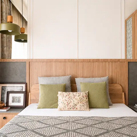 Bedroom with a wood-panelled headboard wall, mustard-green dome pendant lights, and a bed styled with olive green and floral cushions on a block-print quilt.