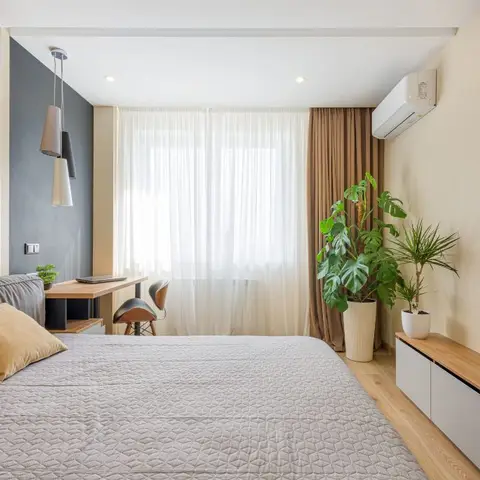 Bedroom with a wood-panelled headboard wall, grey upholstered bed, built-in study desk by the window, wall-mounted TV over a floating credenza