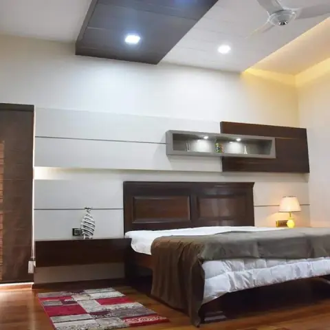 Bedroom with a wood-panelled headboard wall featuring a backlit display niche, a dark wood bed frame, a wood-accented cove ceiling