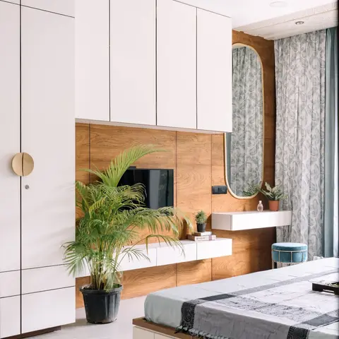 Bedroom with a wood-panelled TV wall and floating console beside an oval brass-framed mirror, paisley-print curtains, and a floor plant.