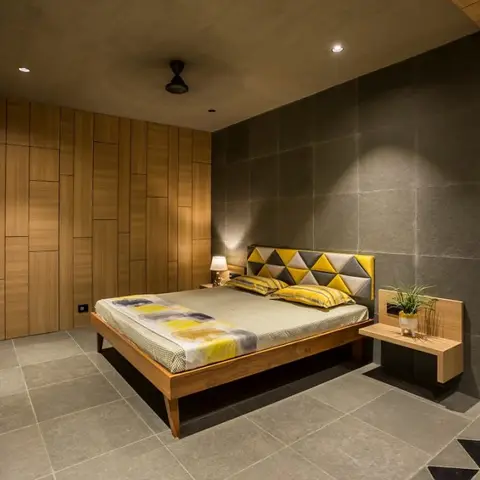 Bedroom with a yellow-and-grey geometric triangular upholstered headboard set against a large-format grey stone-textured wall, a wood-slat wardrobe wall