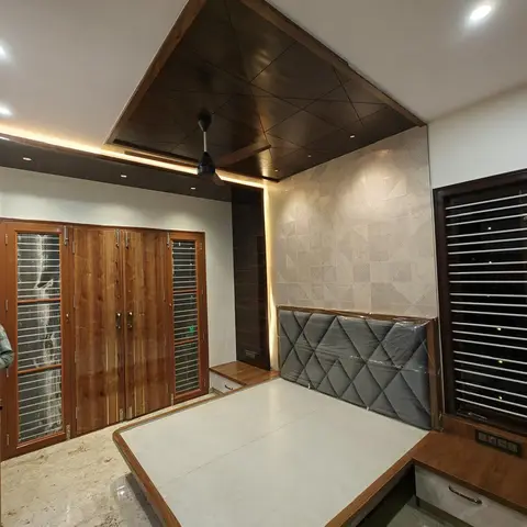 Bedroom with an angled wood-panel ceiling in a diamond lattice pattern, cove lighting, a grey diamond-tufted headboard still wrapped in protective plastic