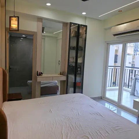 Bedroom with an attached bathroom, a glass-front display wardrobe holding handbags, dressing mirror, and a linear-lit false ceiling.