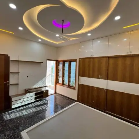 Bedroom with an elaborate swirl-pattern POP false ceiling featuring gold cove lighting and a central purple accent light