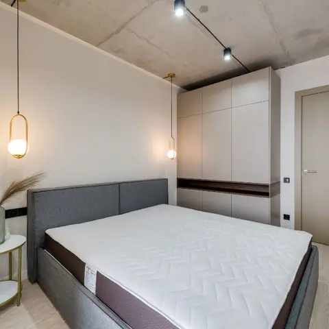 Bedroom with an exposed concrete ceiling, track lighting, twin pendant lamps and a full-height matte wardrobe wall.