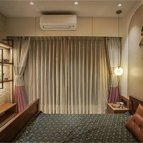 Bedroom with an exposed white-brick wall, floating wood shelves, and pink-hemmed curtains flanking a globe pendant light beside the bed.