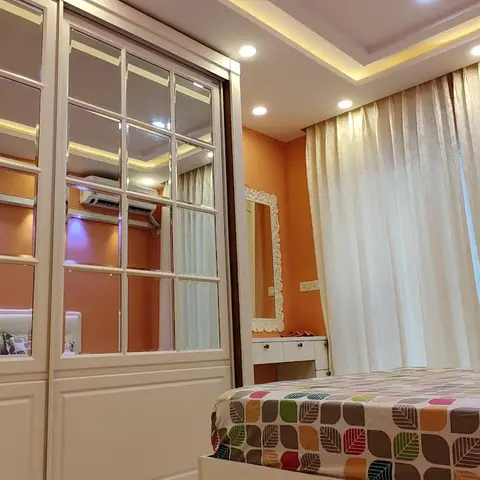 Bedroom with an orange accent wall, a full-height mirrored sliding wardrobe, a cove-lit tray ceiling and an ornate white dressing mirror beside sheer curtains.