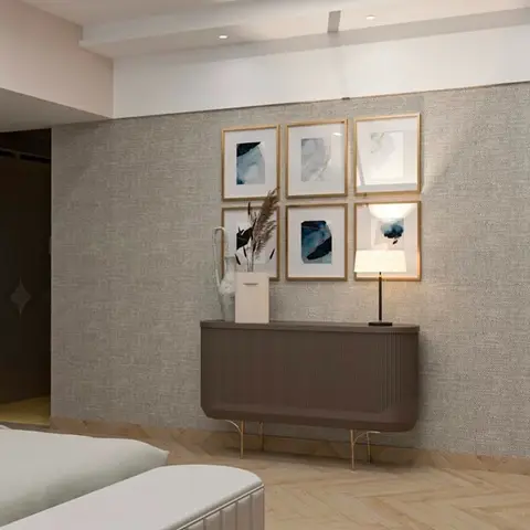 Bedroom with an upholstered grey fabric wall behind a six-piece framed art gallery, a fluted taupe console on brass legs, a table lamp