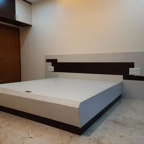 Bedroom with an upholstered platform bed against a wood-veneer wardrobe wall, a fabric-upholstered headboard panel with dark wood accent stripes