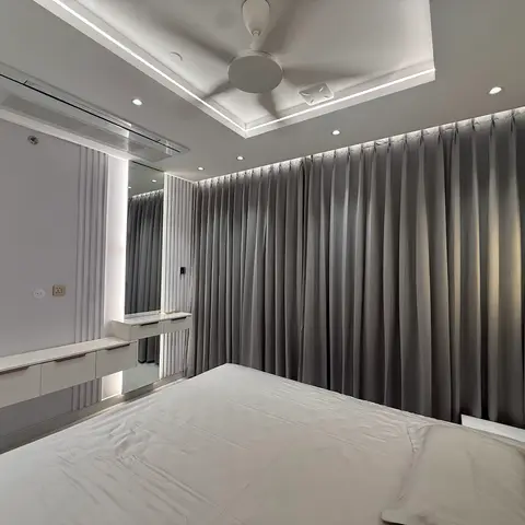 Bedroom with floor-to-ceiling grey curtains, a cove-lit tray ceiling, and a floating white dressing console with mirror.