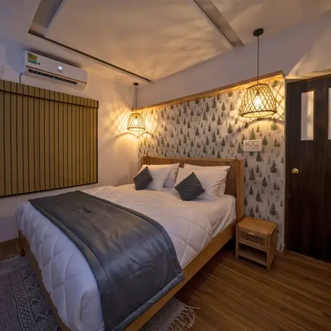Bedroom with pine-tree print wallpaper behind a woven cane-rattan headboard, two woven-basket pendant lights, a bamboo roller blind and warm wood flooring.