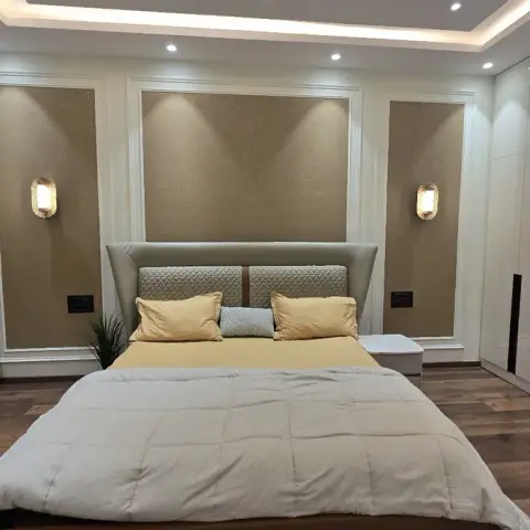 Bedroom with three gold-flecked textured panels framed in white moulding behind a grey wing headboard, twin lantern sconces at pillow height