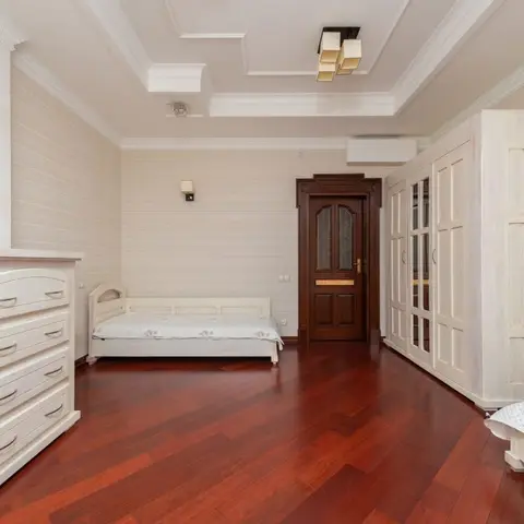 Bedroom with two matching white-wash single beds, a tall whitewashed wardrobe and rich dark-red herringbone-toned wood flooring