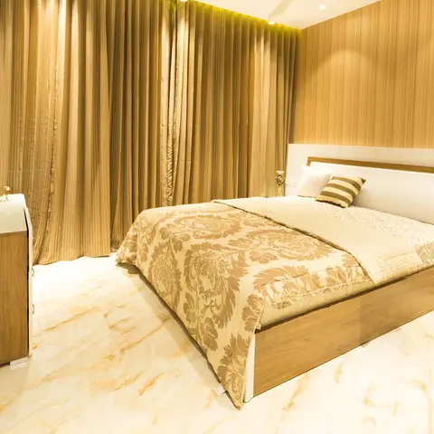Bedroom with wood-veneer strip panelling behind the bed, marble flooring, and heavy gold damask curtains.