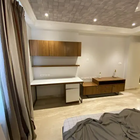 Bedroom work wall with a white desk top slung between teak overhead cabinets and a floating shelf, a teak media console on a slim black frame