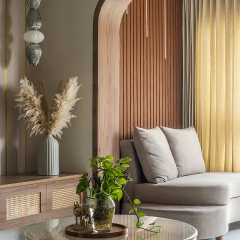 Beige armless lounge chair set into a walnut-framed arched niche of vertical fluted wood with a linen sheer behind it