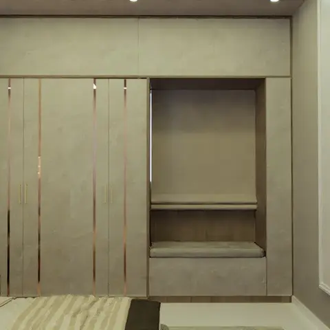 Beige bedroom render where a stone-finish wardrobe run inlaid with rose-gold strips meets a two-tier cushioned alcove