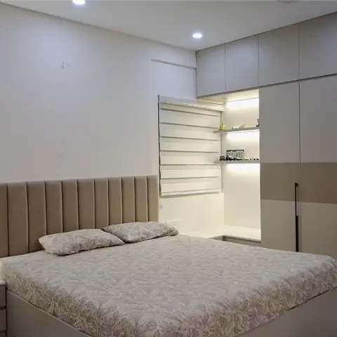 Beige bedroom with a channel-tufted headboard, a round backlit fluted mirror on the side wall, and a full-height loft wardrobe with a lit shelf niche.