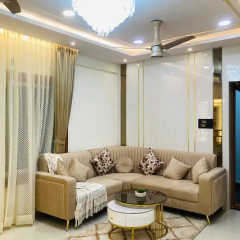 Beige channel-tufted corner sofa under a tiered crystal chandelier, set against a marble-effect wall panel scored with thin brass inlay lines and a cove-lit