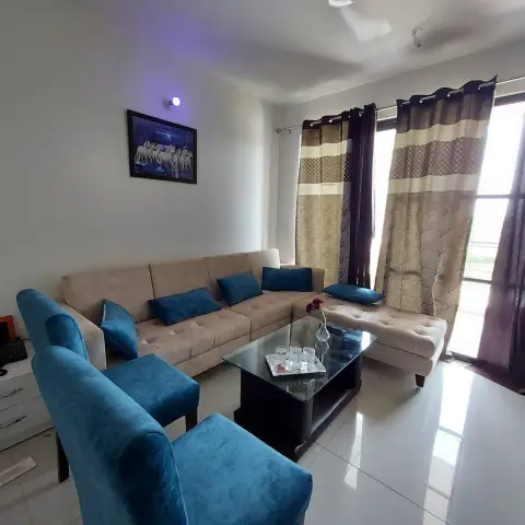 Beige L-shaped fabric sofa with teal cushions facing two teal velvet wing chairs and a dark glass-top coffee table