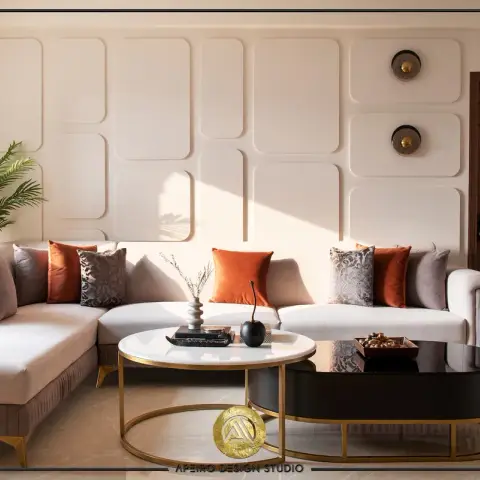 Beige L-shaped sectional with rust and grey cushions against a raised-panel moulded wall fitted with two round brass wall lights