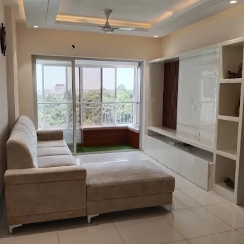 Beige L-shaped sofa facing a white gloss and fluted-wood TV unit with open display shelving, cove-lit ceiling, and a glass door opening to a turf balcony.