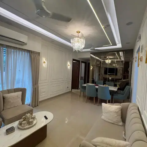 Beige living room seen from behind the channel-tufted sofa, with white moulded panelling and gold sconces on the left wall