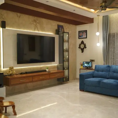Beige marble-clad TV wall with a backlit LED reveal around the screen, a floating teak drawer console and a slim glass display column