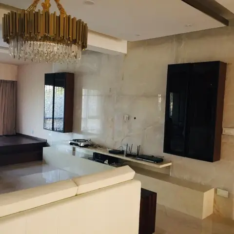 Beige onyx-look slab wall carrying a wall-mounted TV over a floating stone ledge, with a brass-and-crystal tiered chandelier above the cream leather sofa and a