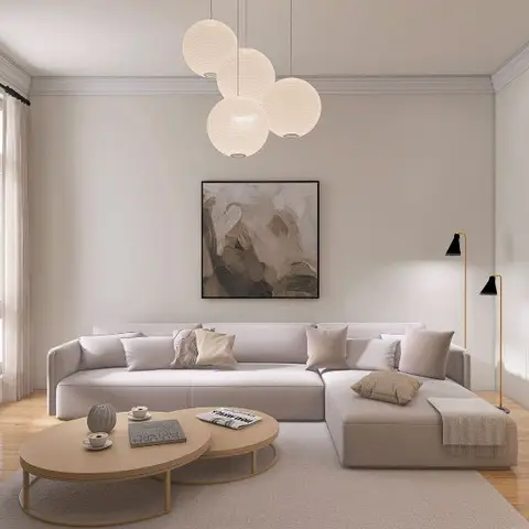 Beige sectional sofa with a cluster of round paper pendant lights and nesting wood coffee tables against a plain wall with a single abstract painting.