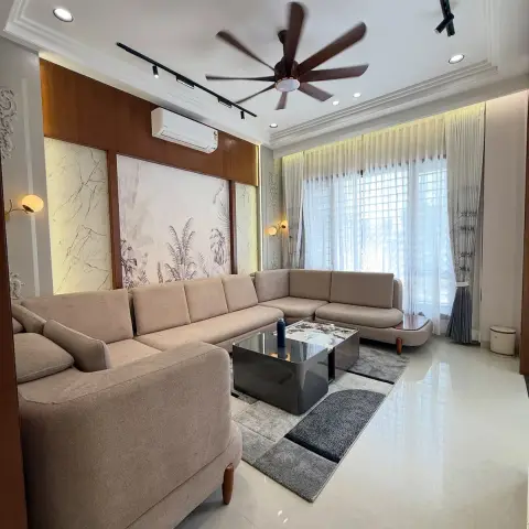 Beige U-shaped sectional and a smoked-mirror coffee table on a grey block rug, facing a backlit tropical-leaf mural framed in teak