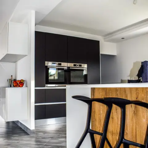 Black and white handleless kitchen tucked under a sloping stair soffit, with two stainless Bosch ovens stacked in the matte black tall bank and three black