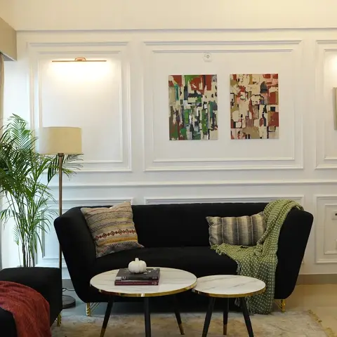 Black channel-tufted velvet sofa against a white wainscoted wall hung with two abstract paintings under brass picture lights