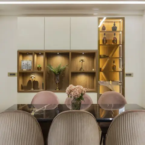 Black marble dining table with blush channel-tufted chairs set against a cream crockery unit of lit walnut niches