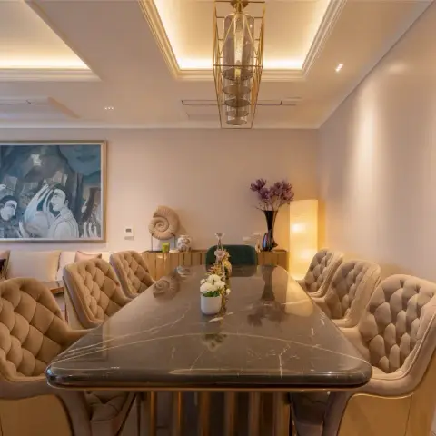Black marble dining top on a fluted brass base with button-tufted beige velvet chairs
